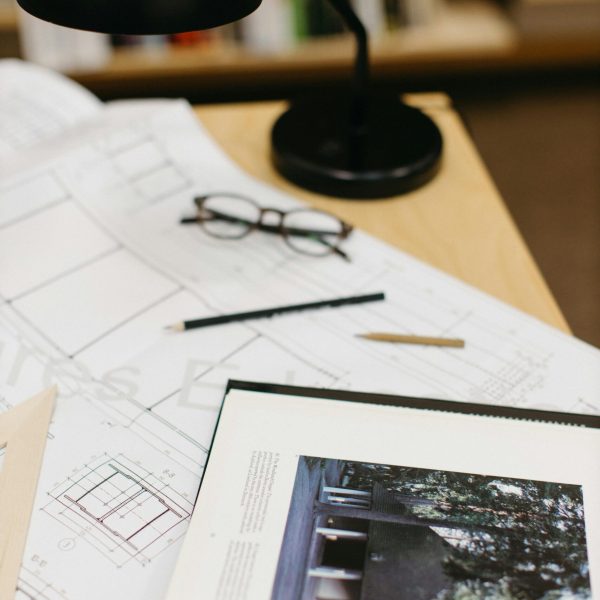 Architect's workspace with blueprints, a book, glasses, and a lamp.